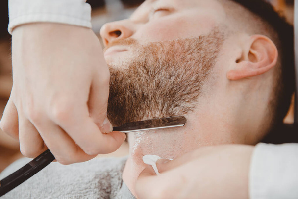 Парикмахер держит бритву для бороды, клиент сидит в кресле
 - Фото, изображение