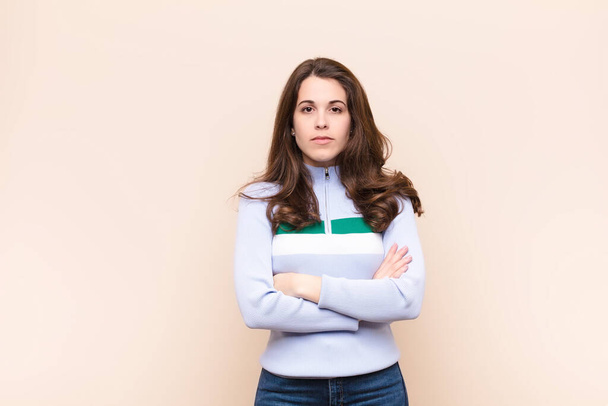 young pretty woman feeling displeased and disappointed, looking serious, annoyed and angry with crossed arms against beige background - Foto, Imagem