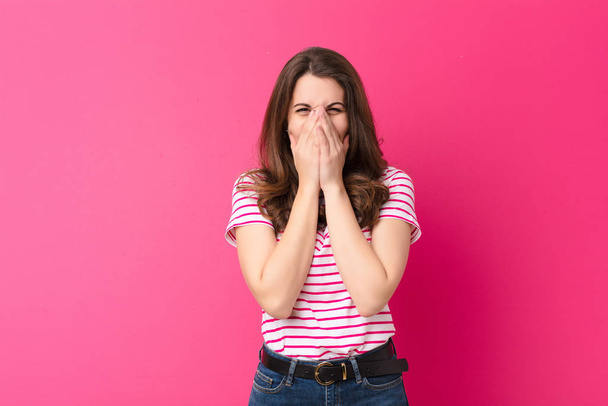young pretty woman looking happy, cheerful, lucky and surprised covering mouth with both hands against pink wall - Foto, Bild
