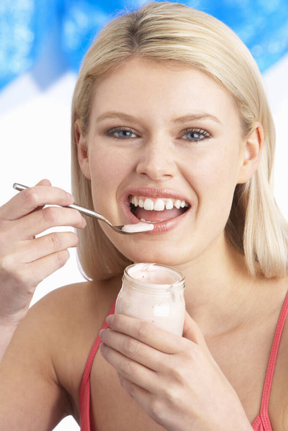 Young Woman Eating Yoghurt In Studio - Foto, afbeelding