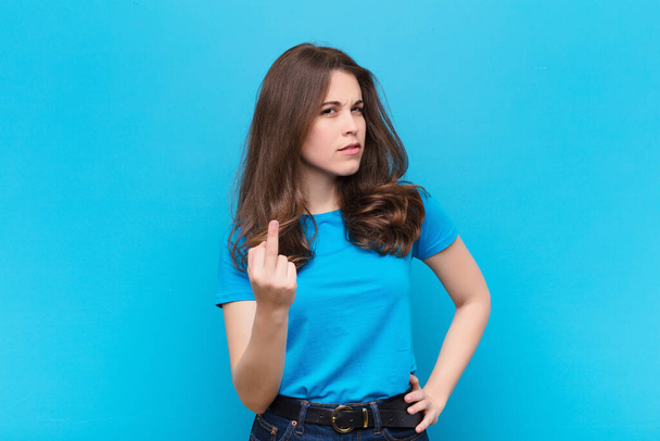jovem mulher bonita sentindo raiva, irritado, rebelde e agressivo, lançando o dedo do meio, lutando contra a parede azul
 - Foto, Imagem