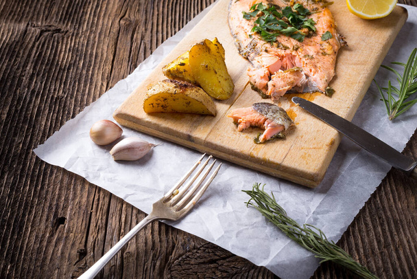 Trout with potateos on wooden board. - Фото, изображение