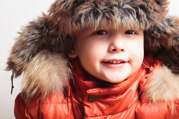 毛皮の帽子に笑みを浮かべて子。ファッション子供。冬のスタイル。小さな男の子。子供たち。オレンジ色の冬のジャケット - 写真・画像