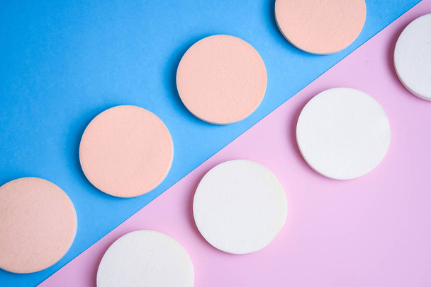 White and beige makeup cosmetic foundation sponges on the blue and pink background, Close up - Фото, изображение