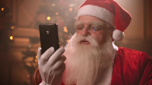 Joulupukki käyttää älypuhelinta ja puhuu videolinkin kautta konferenssin aikana. Joulupukki ja selfie kamera, online-lähetyksiä
. - Materiaali, video