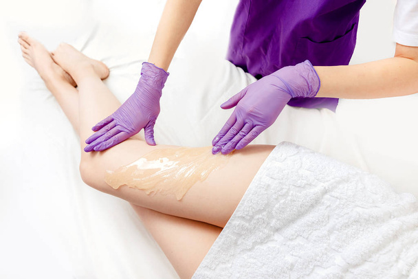 Proces ontharing van benen meisje met suikerpasta in spa salon, witte achtergrond. Shugaring ontharing concept. Bovenaanzicht - Foto, afbeelding