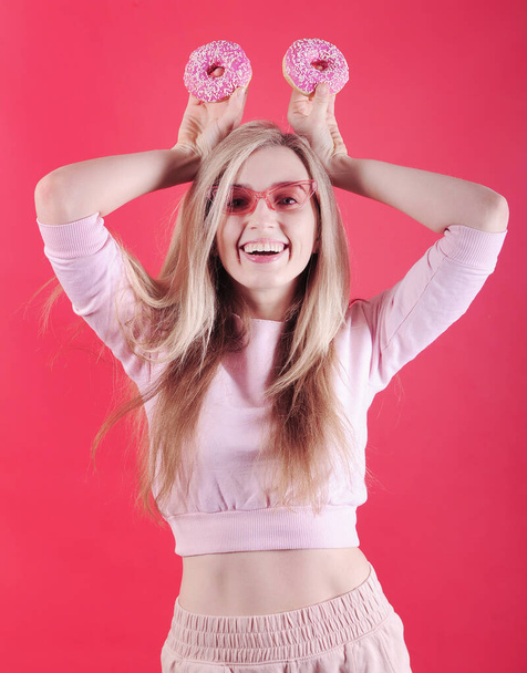 Усміхнена біла жінка з рожевими пончиками позує на червоному тлі в студії
. - Фото, зображення