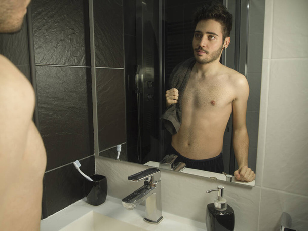 Portrait of handsome caucasian teenager reflection in from of the mirror, smiling with a black towel on his shoulder - Fotografie, Obrázek