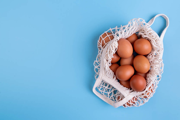 Huevos en un bolso blanco de la red de compras aislado sobre fondo azul vista superior plana con espacio de copia
 - Foto, imagen
