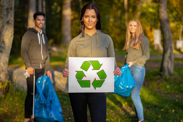 Magabiztos önkéntes nő, aki újrahasznosítási szimbólumtáblát tart - Fotó, kép
