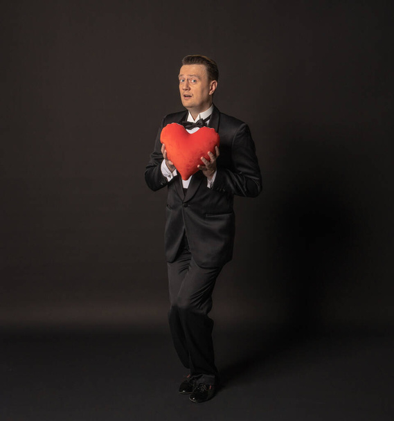 Valentinstag Ehemann mit einem schönen Herzen in einem schwarzen Anzug, schwarzem Hintergrund. - Foto, Bild