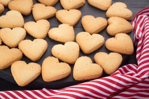 バレンタインデーのために装飾されたハート型のクッキー。テキストのための無料スペース。黒い木製のテーブルの上にジャム付きの2つのハート型のクッキー。黒い木製のテーブルの上にハート型のクッキーを持つ木製のプレート。郵便はがきのようにクッキーの背景 - 写真・画像