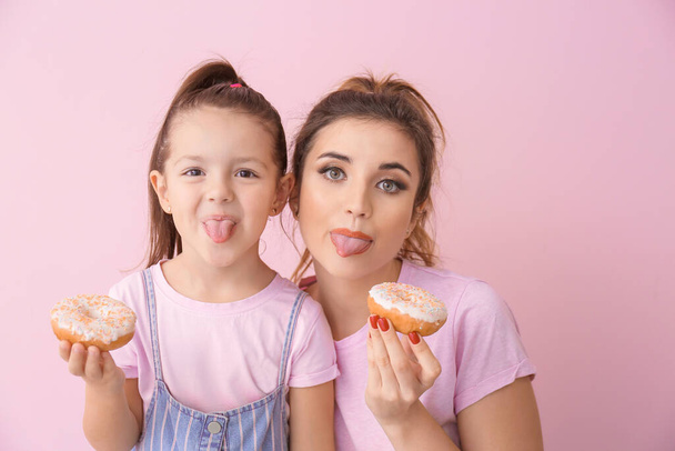 Funny young woman and little girl with donuts on color background - Photo, image