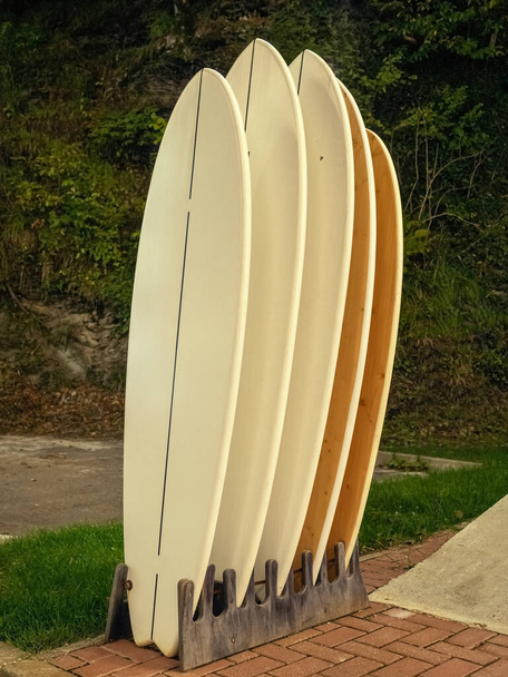 pranchas de surf estão em uma fileira como uma decoração na rua contra uma floresta verde
 - Foto, Imagem
