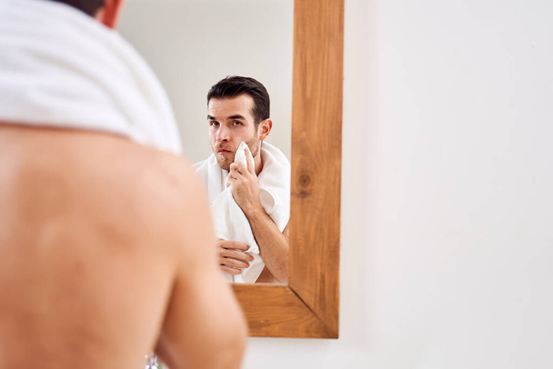 Male wipes his towel while standing by mirror in bath in morning. - Photo, image