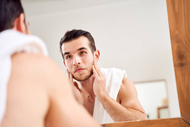 Брюне намыливает лицо и стоит с полотенцем на плечах перед зеркалом в ванной
 - Фото, изображение