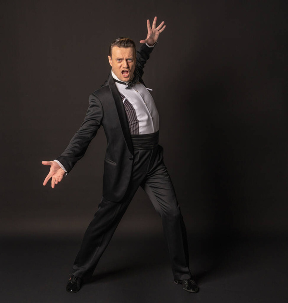 a full-length man on a black background waving his arms in a tuxedo or black  - Foto, imagen