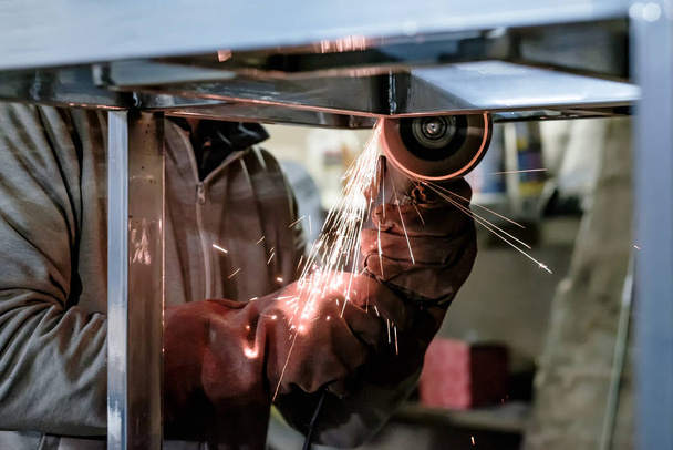 Homem de luvas de proteção corte de metal usando moedor de ângulo fazendo faíscas
 - Foto, Imagem