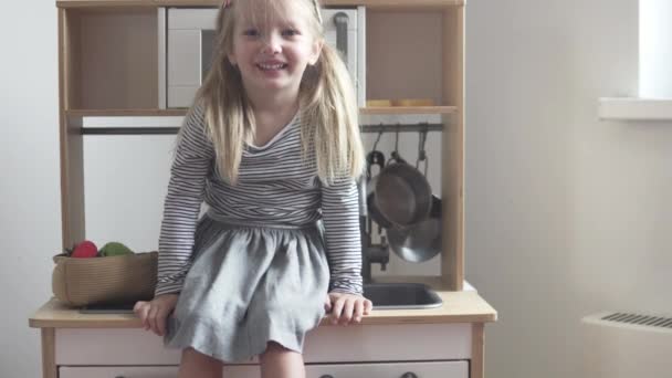 Pikkutyttö istuu lelukeittiössä nauraen.
  - Materiaali, video