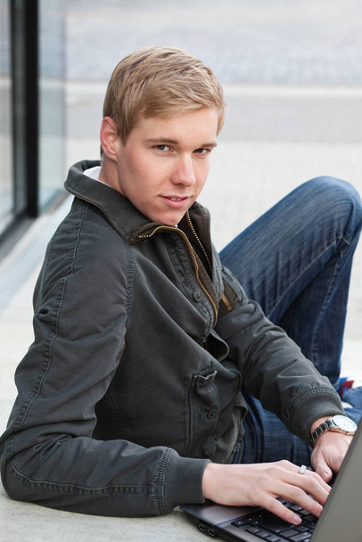 Young blond handsome man with laptop computer in a relaxed pose outdoors - Foto, Imagen