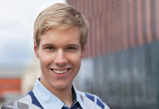 Handsome blond young man smiling outdoors - 写真・画像