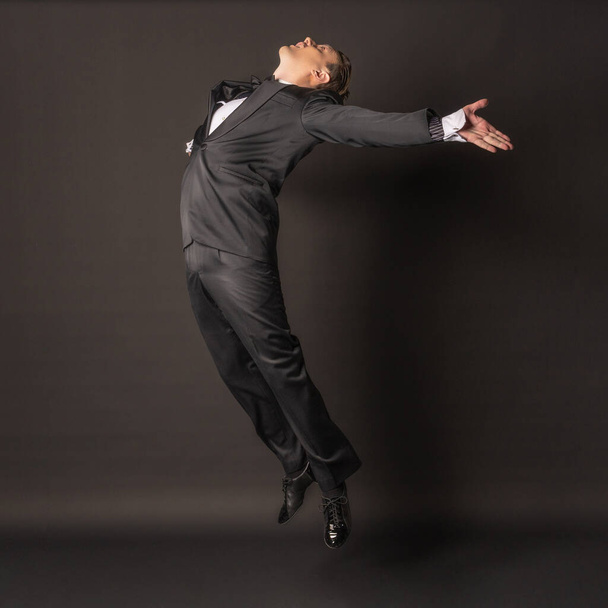 Flying in the air a man on a black background in a tuxedo with wide open hands - 写真・画像