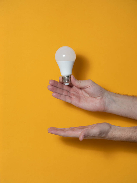 The hand of a man holding a light bulb for innovation and creative concept. Light bulb in hand on a yellow background. Empty space for your text - Photo, image