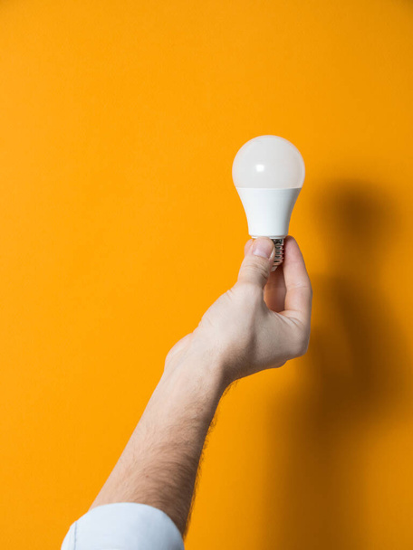 The hand of a man holding a light bulb for innovation and creative concept. Light bulb in hand on a yellow background. Empty space for your text - Fotoğraf, Görsel