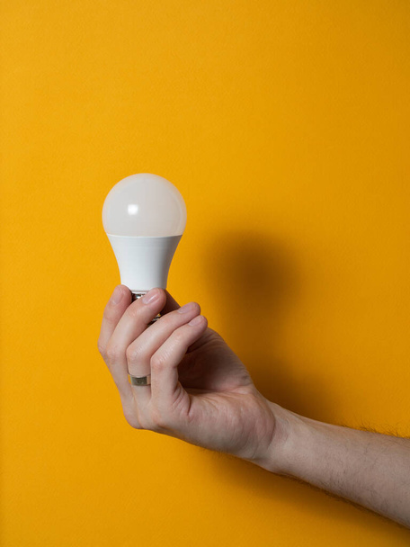 The hand of a man holding a light bulb for innovation and creative concept. Light bulb in hand on a yellow background. Empty space for your text - Photo, image