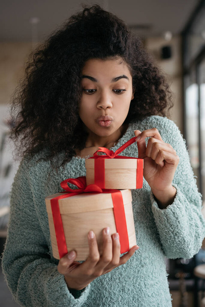 Portret szczęśliwej emocjonalnej kobiety otwierającej pudełko prezentów. młody Afroamerykanin dziewczyna gospodarstwa prezent urodzinowy - Zdjęcie, obraz