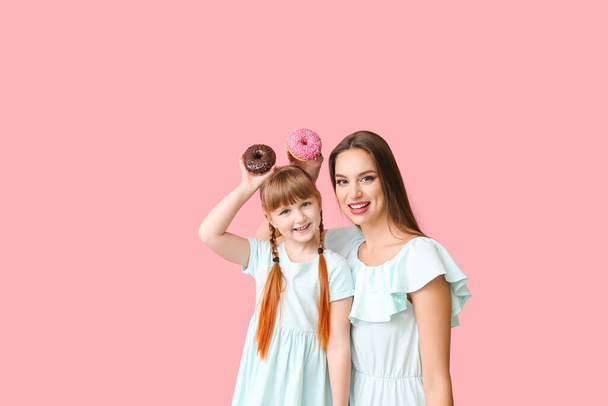 Όμορφη νεαρή γυναίκα και μικρό κορίτσι με ντόνατς στο φόντο χρώμα - Φωτογραφία, εικόνα