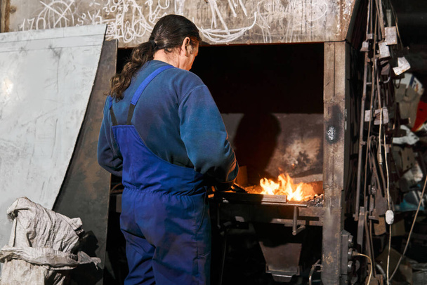 ο σιδεράς θερμαίνει ένα κομμάτι εργασίας στον κλίβανο - Φωτογραφία, εικόνα