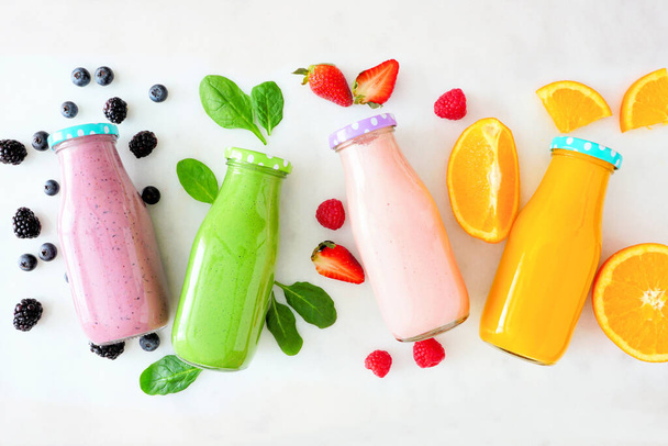 Assorted healthy smoothies in bottles with ingredients. Top view flat lay against a white marble background. Blueberry, green, strawberry, and orange. - Photo, Image