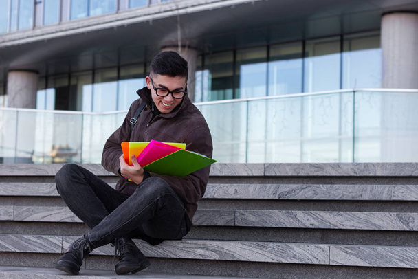 young male Asian student sitting on steps of University with books smiling  - Фото, зображення