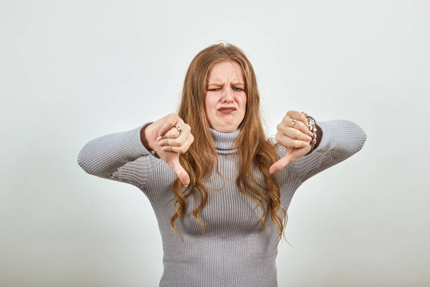 uma jovem mulher ruiva bonita em camisola cinza coloca os polegares para baixo
 - Foto, Imagem