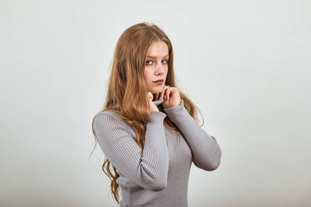 женщина в сером свитере регулирует свою одежду воротник на нем с уверенным взглядом
 - Фото, изображение