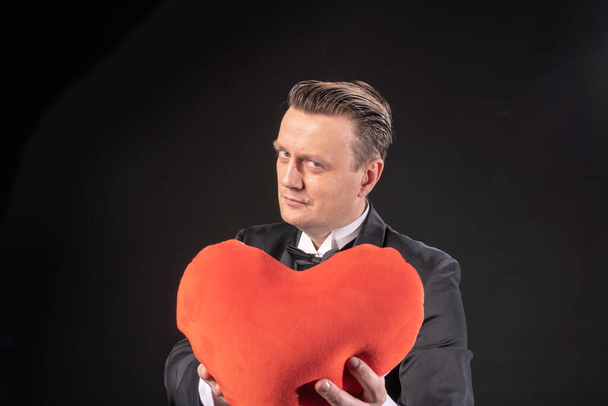 Valentines day husband with a beautiful heart in a tuxedo, black background.  - Fotó, kép