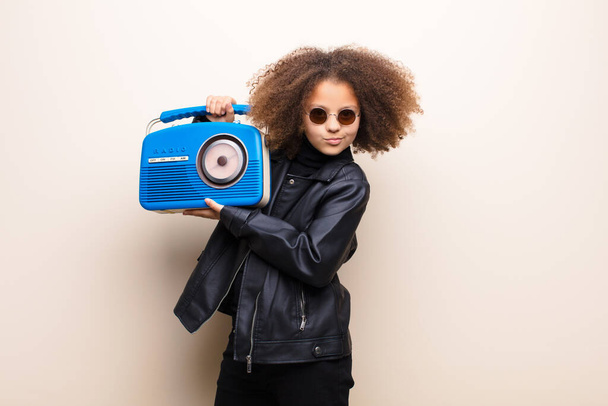 african american little girl  against flat wall listening music with a oldfashioned radio - Foto, Bild