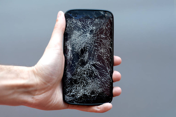 Smartphone with broken screen in hand on grey background. - Photo, Image
