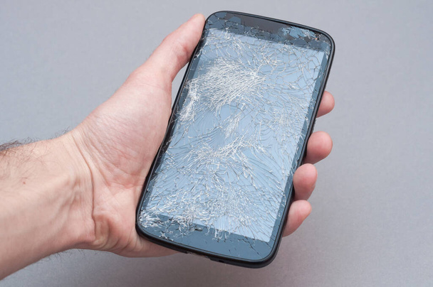 Smartphone with broken screen in hand on grey background. - Photo, image