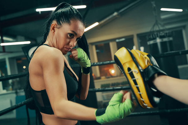 Sportovní žena při tréninku boje na boxerském ringu se zelenými obvazy na rukou, boxovací cvičení s trenérem - Fotografie, Obrázek