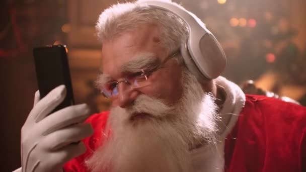 Ένας ηλικιωμένος με λευκή γενειάδα ακούει μουσική με στολή Αϊ Βασίλη παραμονή Χριστουγέννων. Άγιος Βασίλης στο νέο έτος - Πλάνα, βίντεο