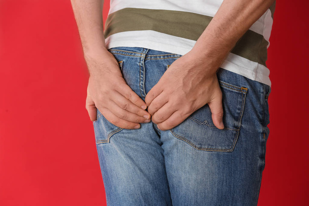 Man suffering from hemorrhoid on red background, closeup - Foto, immagini