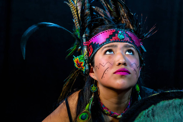 close up of young woman Teotihuacana, Xicalanca - Toltec in black background, with traditional dress dance with a trappings with feathers and drum - Photo, Image