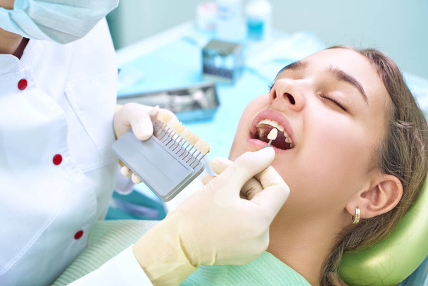 Krásný úsměv a bílé zuby mladé ženy. Odpovídající odstíny implantátů nebo proces bělení zubů. Paleta zubů. - Fotografie, Obrázek