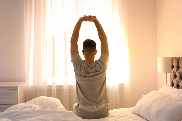 若い男が家でベッドの上で、後ろからの眺めストレッチ。ゆっくり朝 - 写真・画像