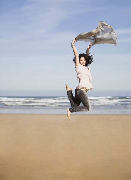 beautiful happy young girl running and jumping over a windy beach with a blowing scarf - Fotografie, Obrázek
