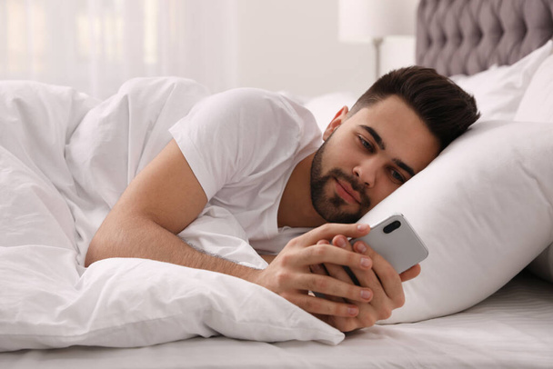 Young man addicted to smartphone in bed at home - Fotografie, Obrázek