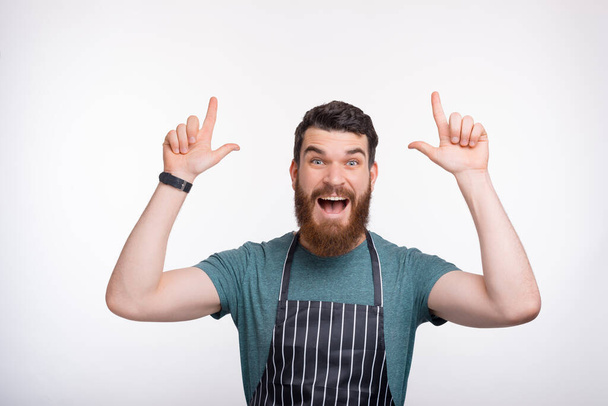 Photo of amazed bearded Chef pointing at copyspace over white background - Photo, Image