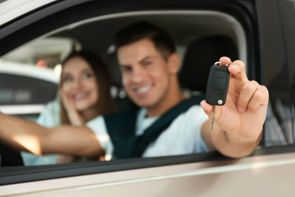 Happy couple sitting in modern car at dealership, focus on hand with key - Photo, image
